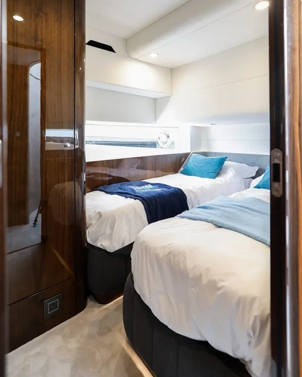 Modern yacht cabin with twin beds, blue and grey decor, bedside table, and ambient lighting, showcasing luxury interior design.